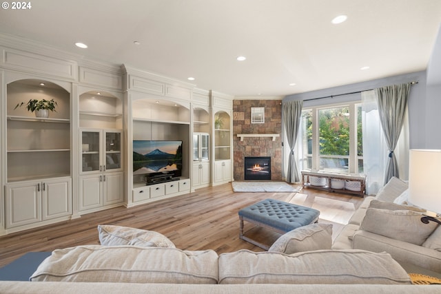 living room with a fireplace, light hardwood / wood-style flooring, built in shelves, and ornamental molding