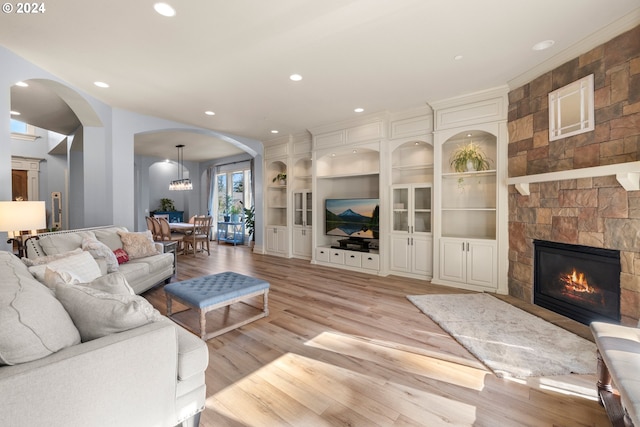 living room with a stone fireplace, light hardwood / wood-style floors, ornamental molding, and an inviting chandelier