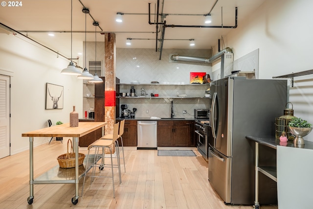 kitchen featuring appliances with stainless steel finishes, backsplash, sink, decorative light fixtures, and light hardwood / wood-style flooring