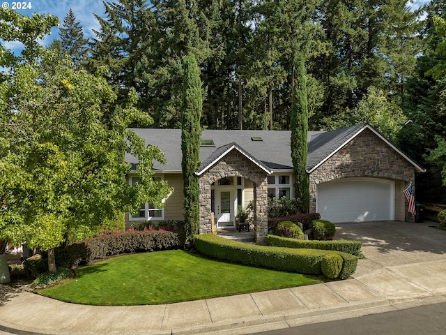 view of front of home featuring a front yard, stone siding, roof with shingles, an attached garage, and driveway