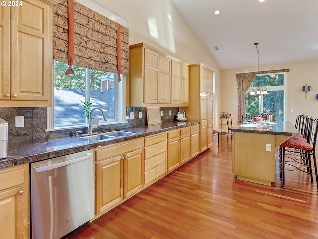 kitchen with hanging light fixtures, a kitchen island, a breakfast bar, stainless steel dishwasher, and sink