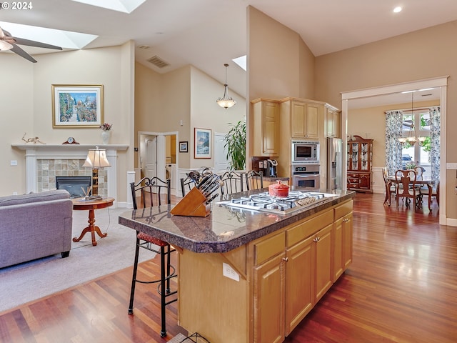 kitchen with light brown cabinetry, a kitchen bar, a kitchen island, hanging light fixtures, and stainless steel appliances