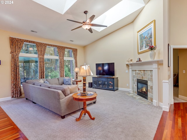 living room featuring a tiled fireplace, hardwood / wood-style flooring, a skylight, high vaulted ceiling, and ceiling fan