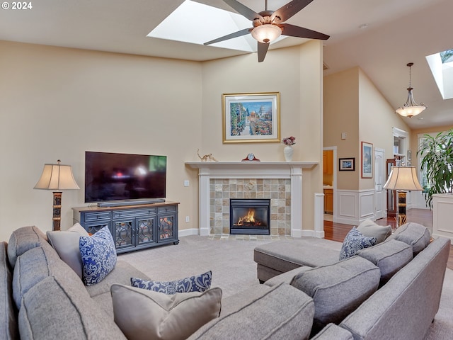 carpeted living room with a tiled fireplace, ceiling fan, a skylight, and high vaulted ceiling