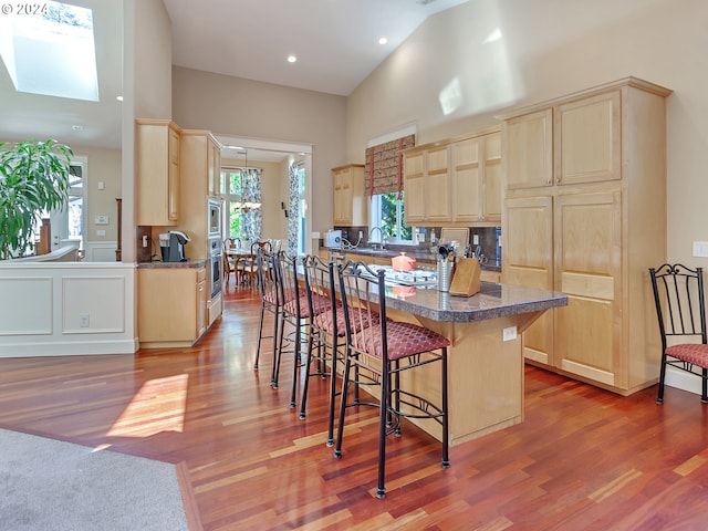 kitchen with appliances with stainless steel finishes, light wood finished floors, light brown cabinets, a kitchen breakfast bar, and high vaulted ceiling