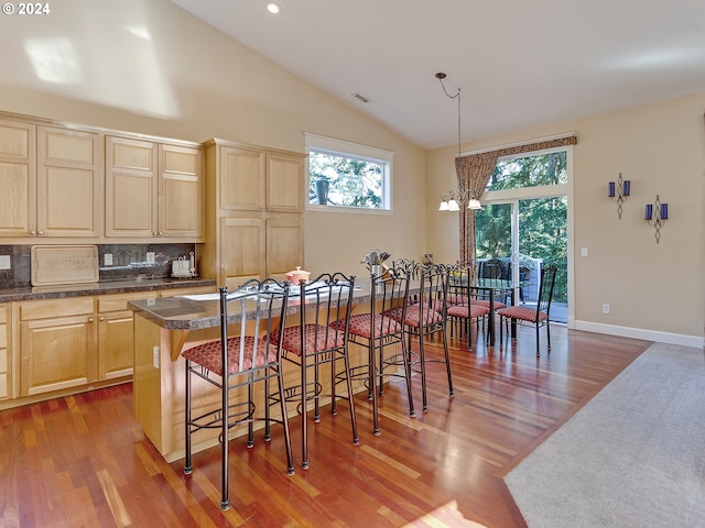 kitchen featuring lofted ceiling, a kitchen island, a kitchen bar, decorative light fixtures, and light brown cabinetry