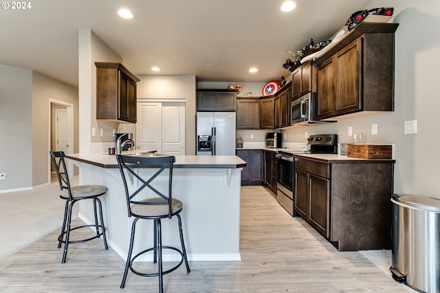 kitchen featuring stainless steel appliances, dark brown cabinetry, sink, a kitchen bar, and light wood-type flooring