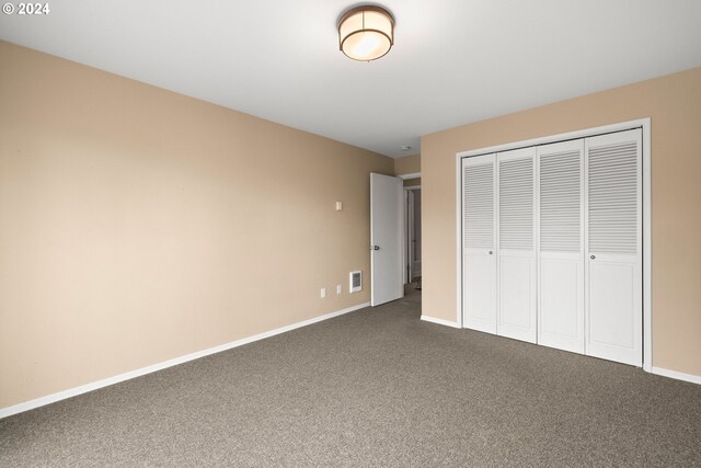 unfurnished bedroom with dark carpet and a closet