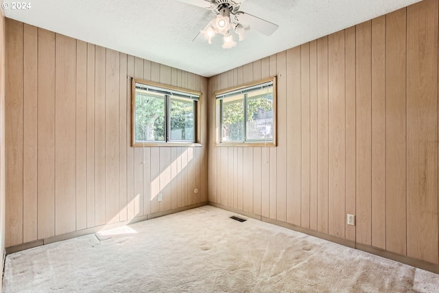 carpeted spare room featuring a textured ceiling, wooden walls, visible vents, baseboards, and a ceiling fan