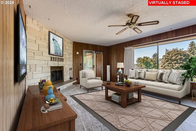 living room with wooden walls, a healthy amount of sunlight, ceiling fan, and a stone fireplace