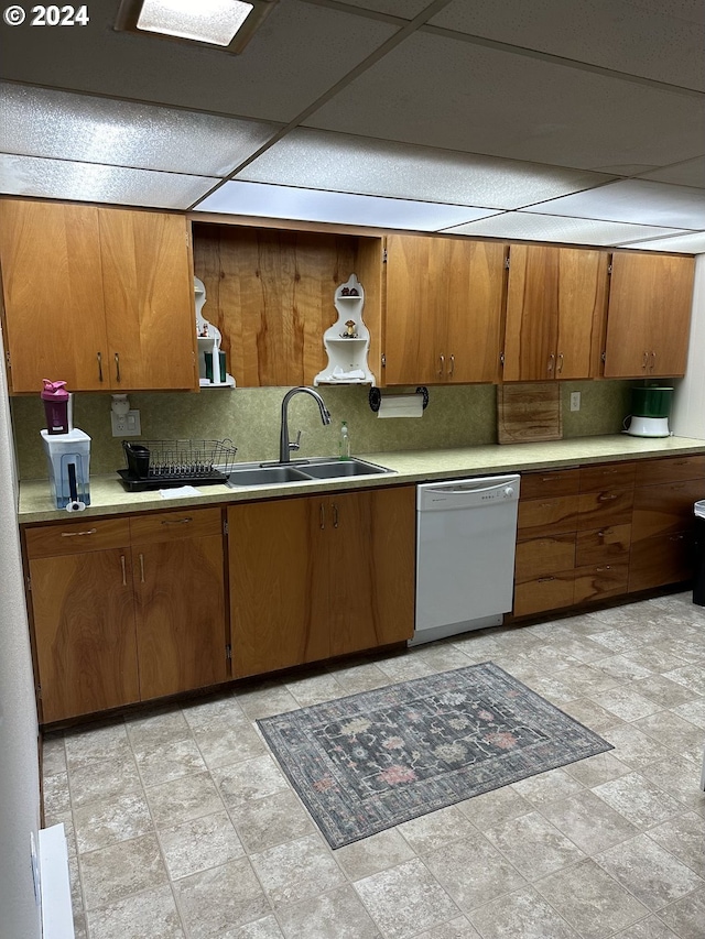 kitchen with light countertops, brown cabinetry, white dishwasher, and a sink