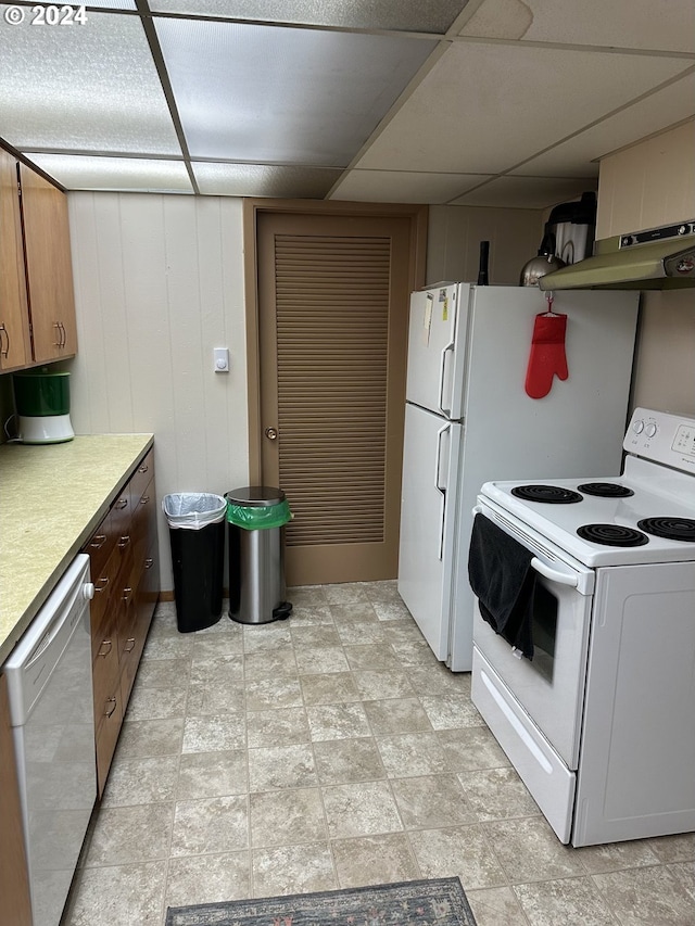 kitchen featuring a paneled ceiling, wooden walls, under cabinet range hood, white appliances, and light countertops