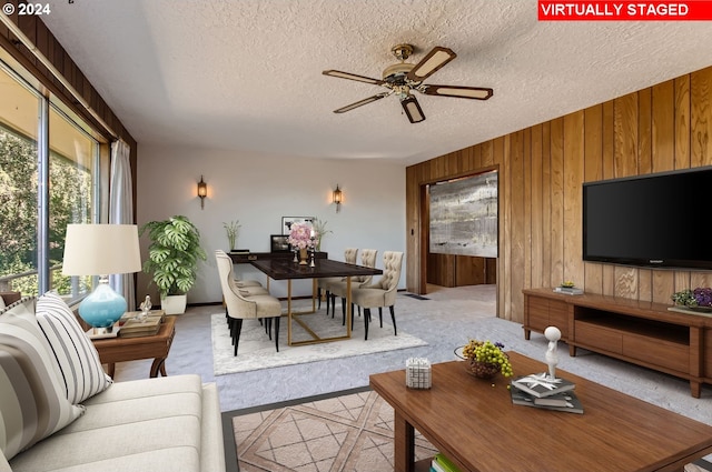 carpeted living area featuring a textured ceiling, wood walls, and a ceiling fan