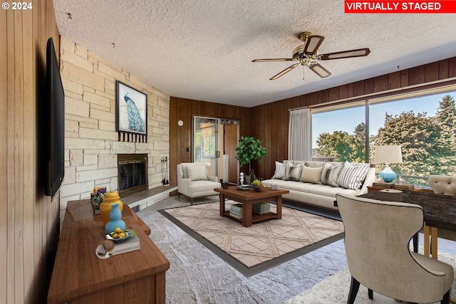 living area with a textured ceiling, wood walls, a fireplace, and a ceiling fan