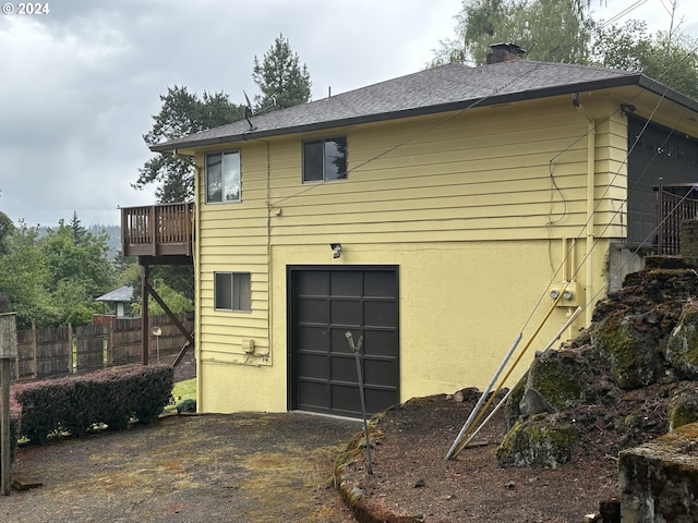 exterior space featuring roof with shingles, a chimney, stucco siding, fence, and a garage