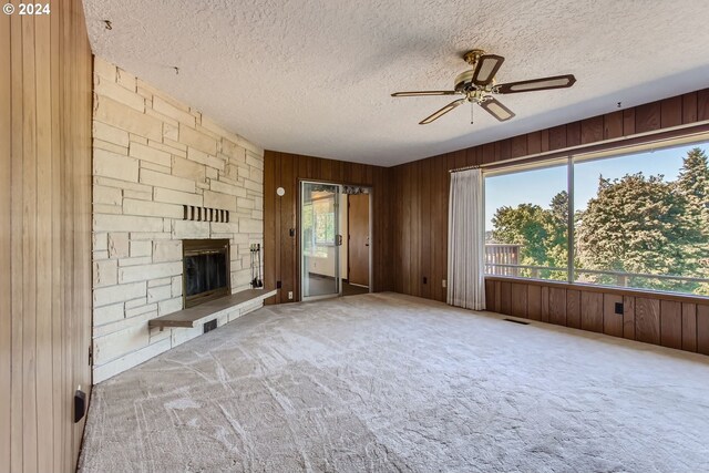 unfurnished living room with a textured ceiling, a fireplace, carpet, ceiling fan, and wooden walls