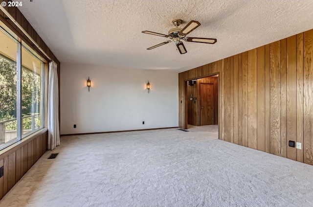 spare room featuring light carpet, wooden walls, visible vents, ceiling fan, and a textured ceiling