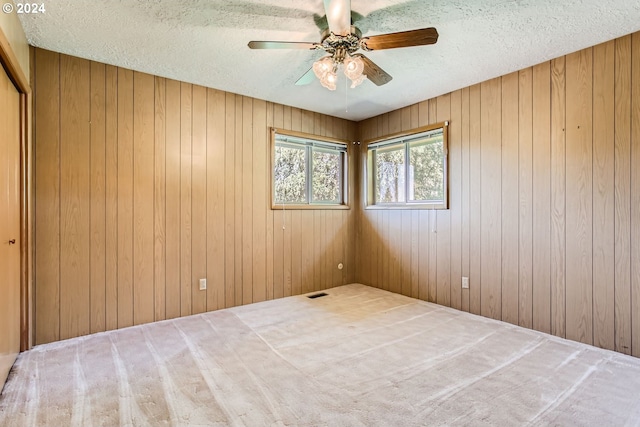 carpeted empty room with ceiling fan, wooden walls, visible vents, and a textured ceiling