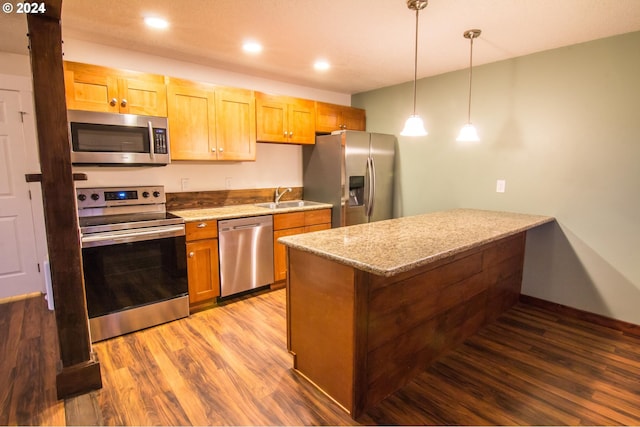 kitchen featuring sink, hanging light fixtures, hardwood / wood-style flooring, light stone countertops, and stainless steel appliances