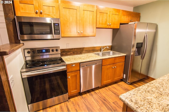 kitchen with appliances with stainless steel finishes, light hardwood / wood-style flooring, sink, and light stone counters