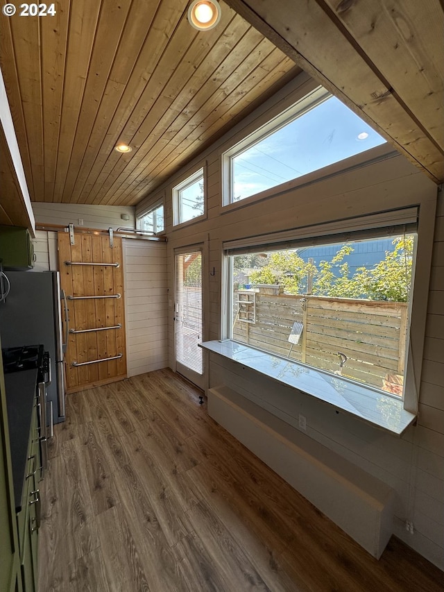 additional living space featuring wood walls, dark hardwood / wood-style floors, wooden ceiling, and a barn door