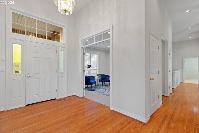 foyer entrance featuring light wood-type flooring, a towering ceiling, and an inviting chandelier