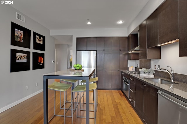 kitchen with dark brown cabinets, stainless steel appliances, light hardwood / wood-style floors, sink, and a breakfast bar