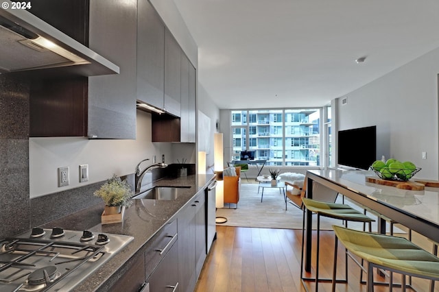 kitchen with stainless steel gas cooktop, wall chimney range hood, sink, floor to ceiling windows, and light hardwood / wood-style floors