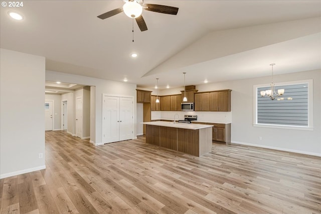 kitchen with lofted ceiling, ceiling fan with notable chandelier, hanging light fixtures, an island with sink, and light hardwood / wood-style floors