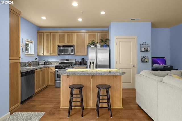 kitchen with sink, appliances with stainless steel finishes, a kitchen breakfast bar, a center island, and wood-type flooring