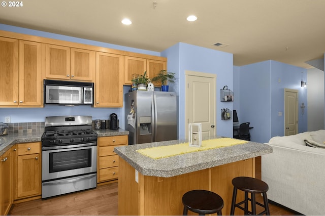 kitchen with appliances with stainless steel finishes, a kitchen breakfast bar, a center island, and hardwood / wood-style floors