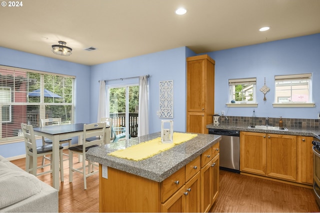 kitchen with sink, tasteful backsplash, stainless steel dishwasher, a kitchen island, and light hardwood / wood-style floors