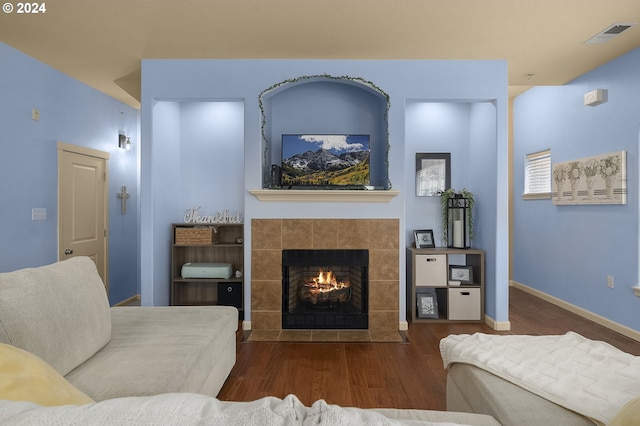 living room featuring a tiled fireplace and dark hardwood / wood-style flooring