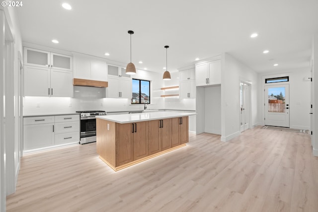 kitchen featuring decorative light fixtures, white cabinets, light wood-type flooring, stainless steel range, and a kitchen island