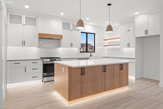 kitchen featuring white cabinets, a center island, hanging light fixtures, stainless steel stove, and light wood-type flooring