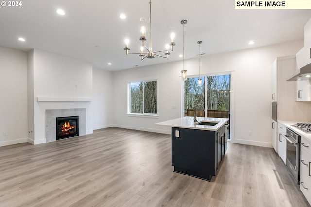 kitchen featuring white cabinets, pendant lighting, sink, a kitchen island with sink, and a tiled fireplace