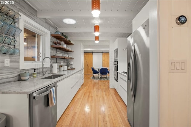 kitchen featuring beamed ceiling, white cabinetry, sink, stainless steel appliances, and a barn door