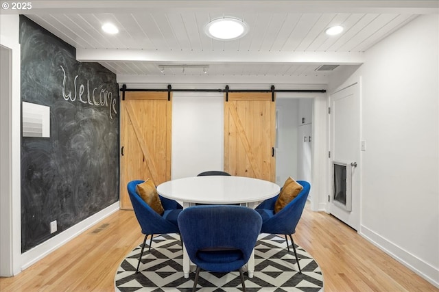 dining space featuring light wood-style floors, a barn door, and beamed ceiling