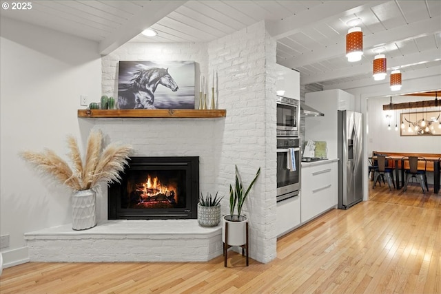 kitchen with white cabinetry, stainless steel appliances, beam ceiling, and light wood-type flooring