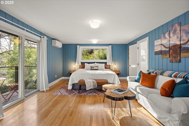 bedroom featuring a wall unit AC, light wood-style floors, multiple windows, and baseboards