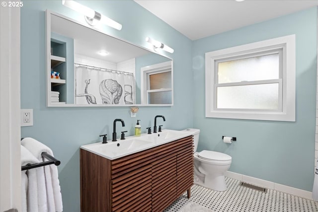 bathroom featuring toilet, a sink, visible vents, baseboards, and double vanity