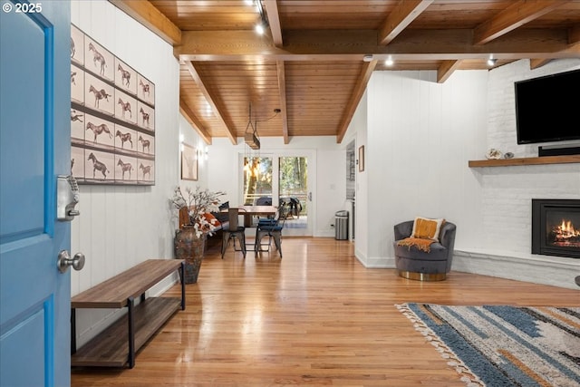 foyer featuring light wood finished floors, wood ceiling, a large fireplace, and beam ceiling