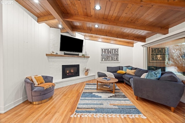 living room with a large fireplace, lofted ceiling with beams, wooden ceiling, and wood finished floors