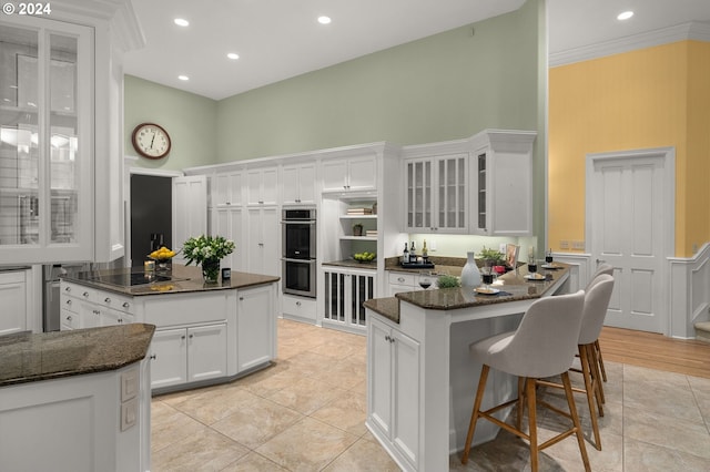 kitchen with double oven, white cabinetry, a center island, and crown molding