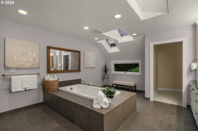 bathroom with vanity, a textured ceiling, lofted ceiling with skylight, a relaxing tiled tub, and tile patterned floors