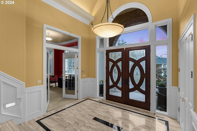 foyer featuring french doors, crown molding, light hardwood / wood-style floors, and a towering ceiling