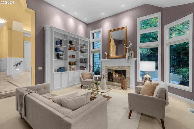 carpeted living room with a stone fireplace, a towering ceiling, and built in features