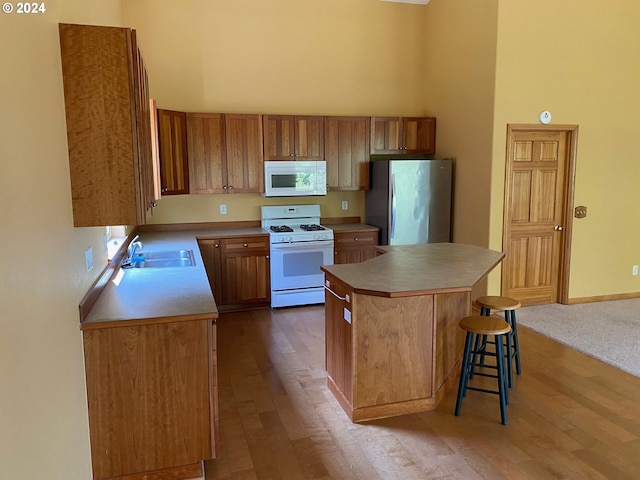 kitchen featuring a towering ceiling, a center island, dark wood finished floors, a sink, and white appliances