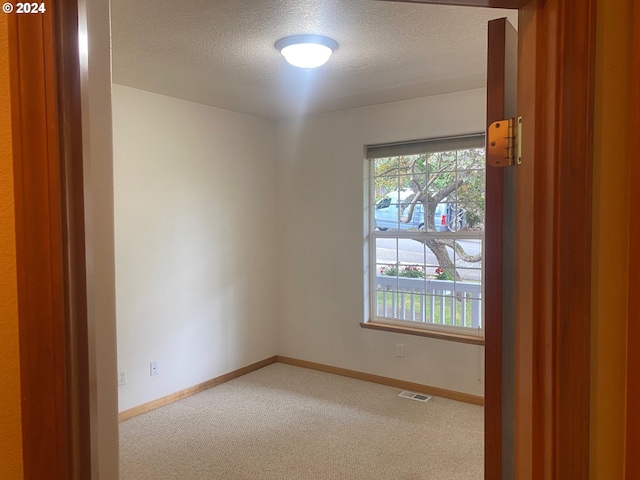 carpeted empty room with visible vents, a textured ceiling, and baseboards