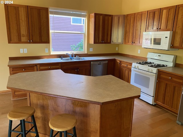 kitchen with brown cabinetry, a sink, a breakfast bar, and white appliances